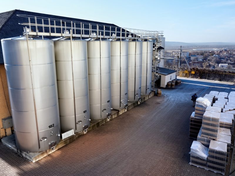 Metal wine storage tanks with dwelling houses on the background in a winery. Wide shot